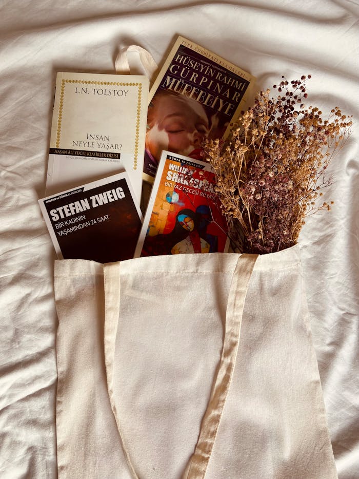 services-02 Beige tote bag filled with classic books and dried flowers on a soft white cloth.