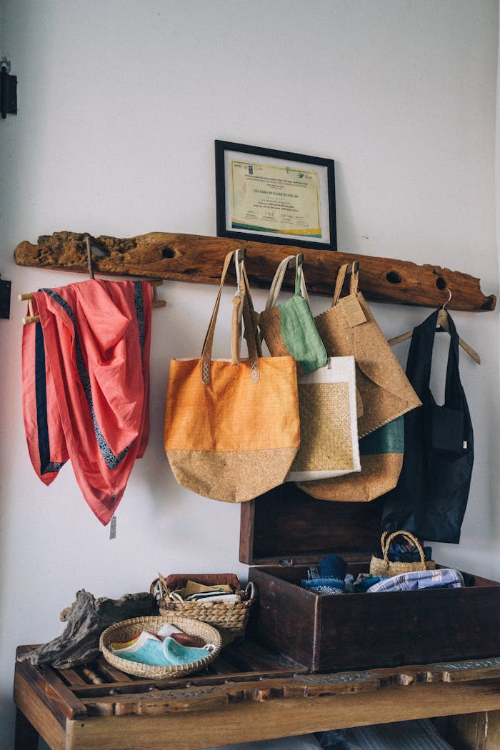 Colorful reusable shopping bags and scarves hang on wooden rack in cozy setting.